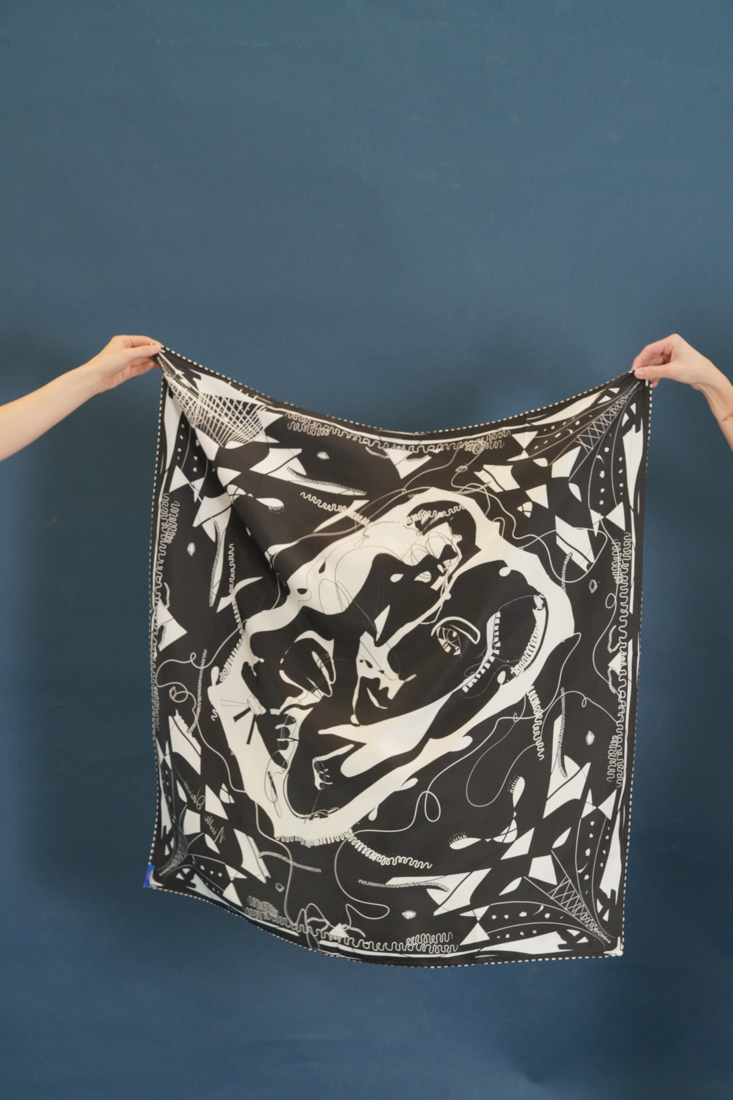 A silk scarf with modern design of a seamstress working on a dress, surrounded by geometrical black and white lines and loose threads.