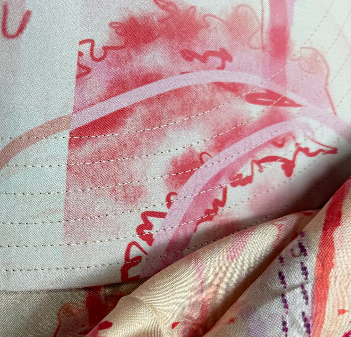 A close-up of a  coral floral hat with a pink and red abstract watercolor print, layered over a matching patterned scarf.