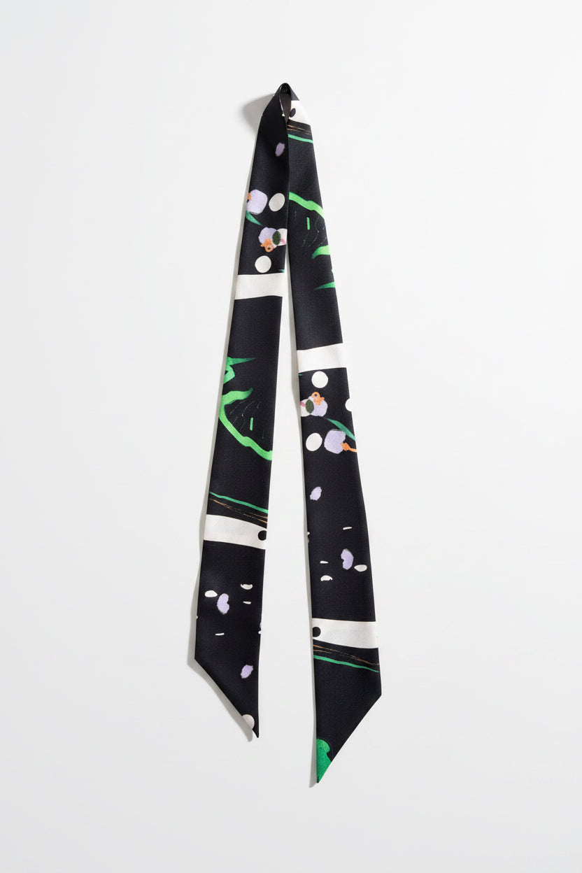 A long necktie with a black base and a modern abstract pattern featuring white stripes, green brushstrokes, and small pink and purple floral details, laid flat on a textured beige fabric background.