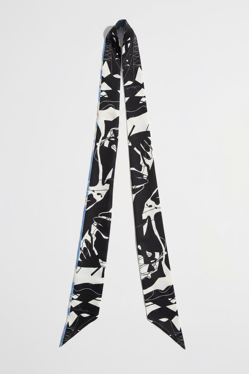 A long silk scarf with a black and white graphic print of stylized faces, displayed against a light gray background.