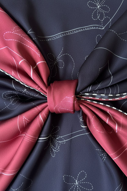 A close-up of a folded silk scarf featuring a black base with white embroidered floral patterns, contrasted by vibrant magenta-black checkered borders 
