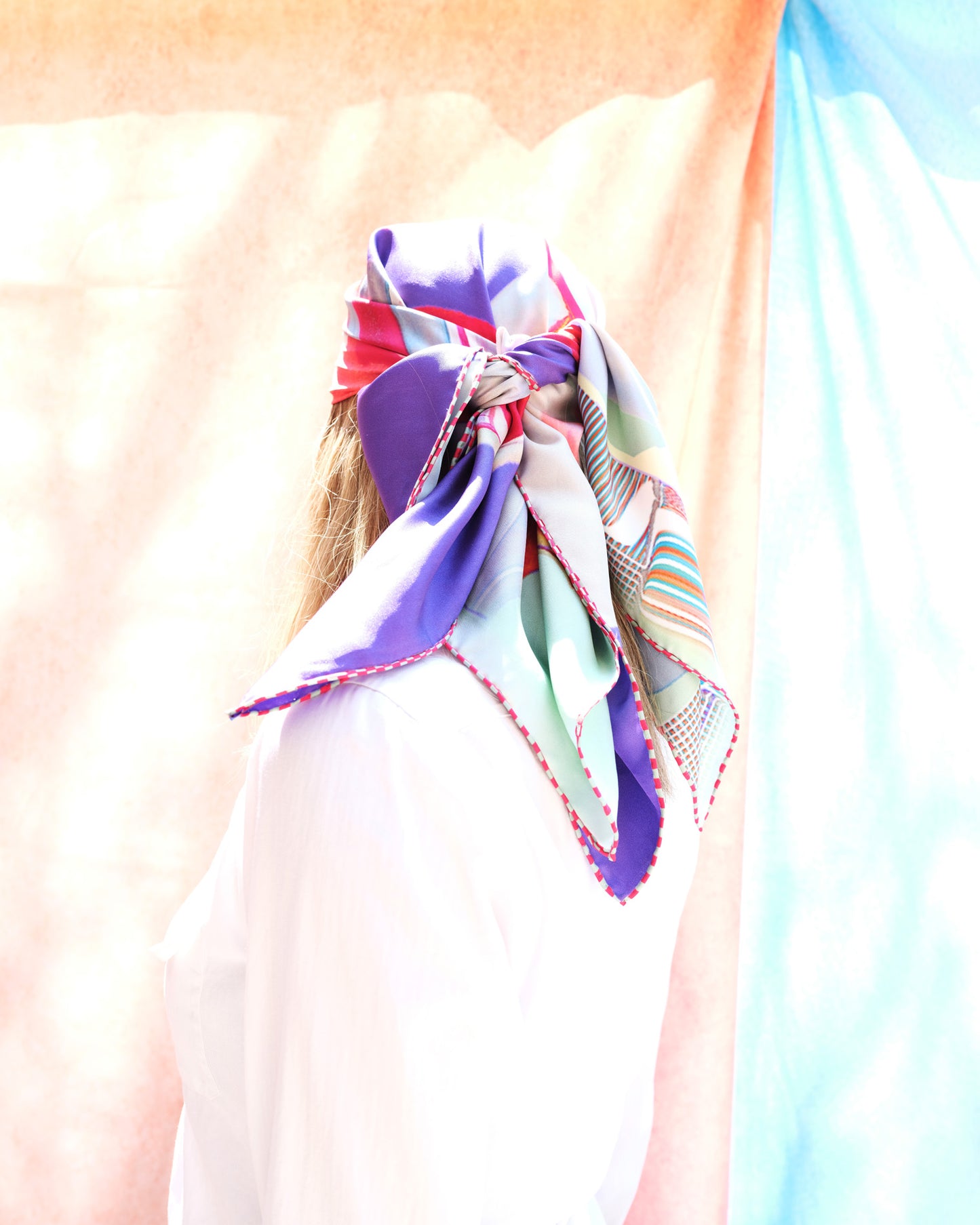 woman wearing a bold color head scarf  with purples pinks, blues, greens  and reds 